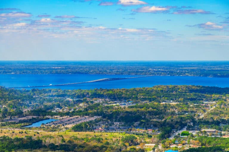 Aerial view of a large lake with surrounding green landscape and cityscape.