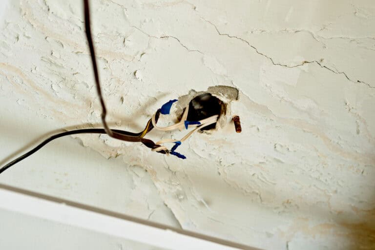 Damaged ceiling with exposed wiring and peeling paint in a house.