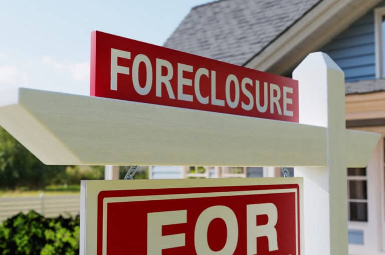 Foreclosure sign in front of a house indicating property is for sale due to foreclosure.