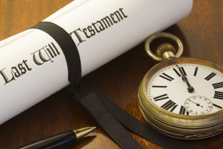 Last Will and Testament document with pocket watch and pen on wooden surface.