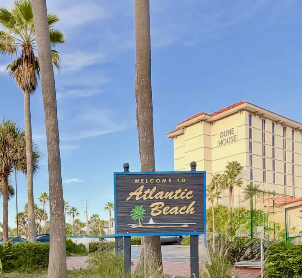 Welcome to Atlantic Beach sign with palm trees and Dune House hotel in background.