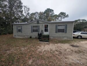 St. Augustine mobile home on a dirt lot with steps to entry.