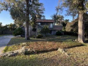 Suburban home with a sloped yard and mature trees in front, driveway on the left.